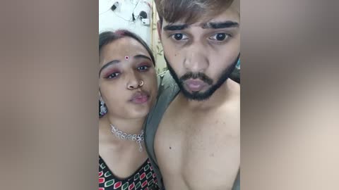 Media: Video of a South Asian couple: a woman with medium skin, dark hair, and traditional jewelry, and a man with light skin, short brown hair, and a beard, both making playful faces.