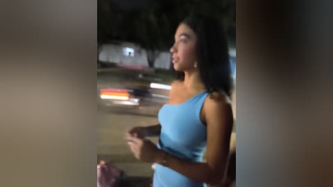 Media: A video shows a young woman with long, dark hair in a light blue dress, holding a pink bag, standing on a street at night with blurred car lights in the background.