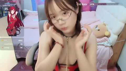 Media: A young, slender Asian woman with glasses and a red top sits in a bedroom, holding a teddy bear. The room is colorful with pink and blue walls.