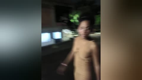 Media: A blurred video of a nude, slender woman with dark skin, medium breasts, and short black hair, walking in a dimly lit, possibly urban, setting with green and blue lights in the background.