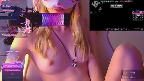 Media: Video of a topless, fair-skinned blonde woman with small breasts, wearing a white mask, sitting in a dimly lit room, holding a microphone, surrounded by various chatroom screens.