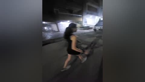 Media: Video of a woman in a black dress and sneakers running away on a dark, wet street at night. She holds a bag. Background shows a chain-link fence, parked cars, and a lit building.