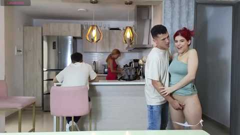 Media: Video of a modern kitchen with a young man and woman in a sexual act; woman is topless with red hair, man has short dark hair, both smiling.