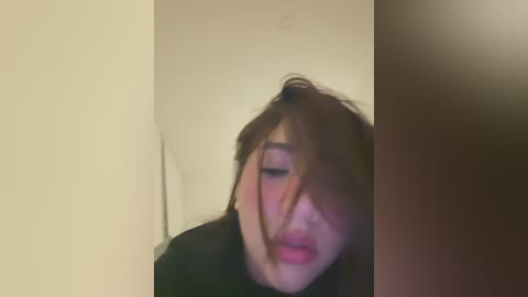 Media: A blurry video of a young Asian woman with shoulder-length brown hair, wearing black clothing, caught in a moment of shock or surprise, with a white wall and a brown door in the background.