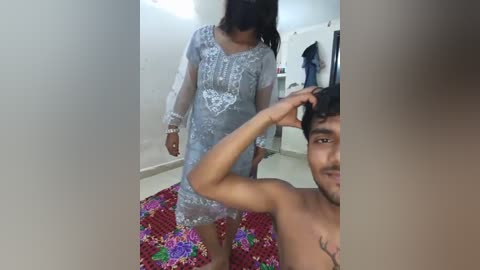 Media: A video of a topless young man with a small tattoo on his chest, wearing a floral-patterned skirt, standing in a room with a woman in a see-through dress.