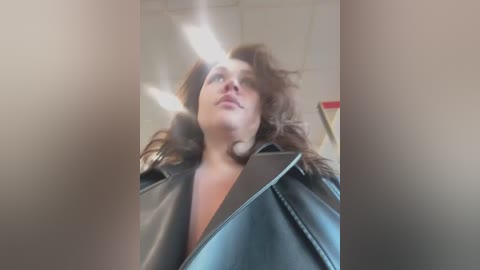 Media: A video of a young woman with shoulder-length, curly brown hair, wearing a black leather jacket, captured from a low angle, with a blurred, indistinct background.