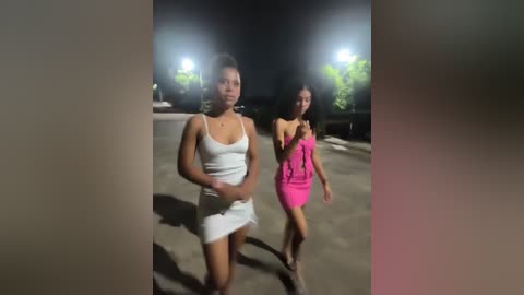 Media: Video of two women walking at night, one in a white dress, the other in a bright pink dress, under streetlights in a suburban setting.