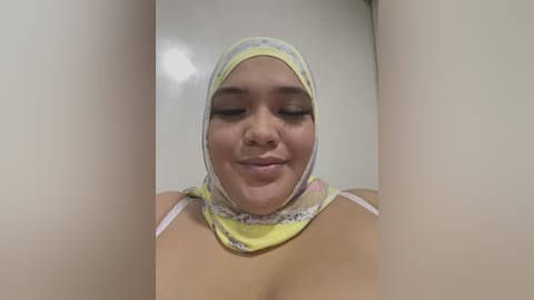 Media: Video of a smiling, light-skinned woman with medium-length hair, wearing a yellow hijab and white spaghetti straps, set against a plain, white background.