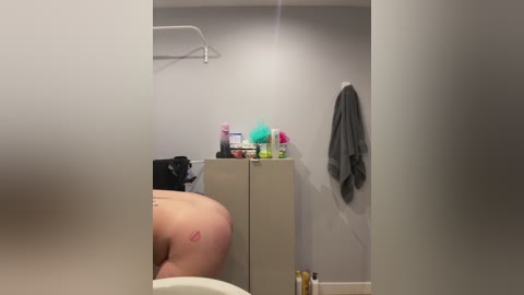 Media: Video of a bathroom mirror reflecting a person's bare back with a tattoo, beige cabinets, towels, and toiletries.