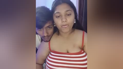 Media: Video of a South Asian woman with medium skin tone, wearing a red and white striped tank top, and a man with dark skin, both smiling.