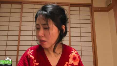 Media: Video of an Asian woman with long black hair, wearing a red floral kimono, looking distressed. She's indoors, with wooden shoji screens in the background.