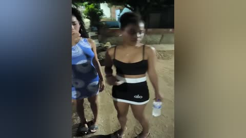 Media: Video of two women in casual sportswear walking on a sandy path at night, one holding a water bottle.