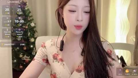 Media: A video of an Asian woman with long brown hair, wearing a floral top, sitting in front of a decorated Christmas tree, using a smartphone.