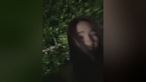 Media: A dimly lit video features a blurred, shadowy figure partially obscured by dense green foliage, creating an eerie, mysterious atmosphere.