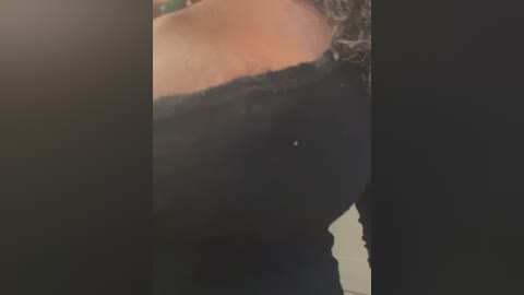 Media: A close-up video of a person's upper body wearing a black, off-shoulder top with lace trim. The background is dark, making the subject's fair skin and black garment stand out.