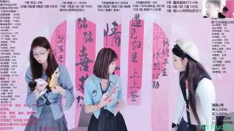 Media: Video of three young Asian women, each in different school uniforms, holding small dolls, standing against a pink backdrop with Chinese characters. The scene has a playful, vibrant atmosphere.