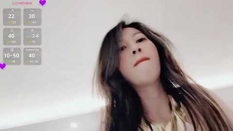 Media: A video of an Asian woman with long, dark hair, wearing a beige top, captured in a modern indoor setting with a white background and a digital display showing her age as 22.