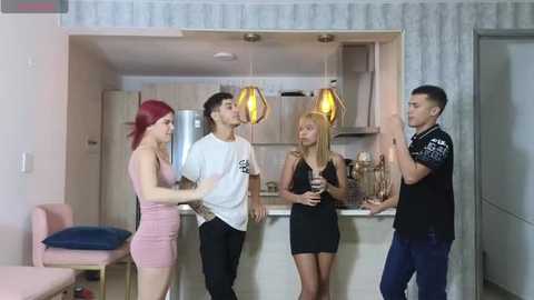 Media: Video of four young adults in a modern kitchen, two men and two women, discussing something; one woman wears a tight pink dress, one man a black shirt, and the others in casual attire.