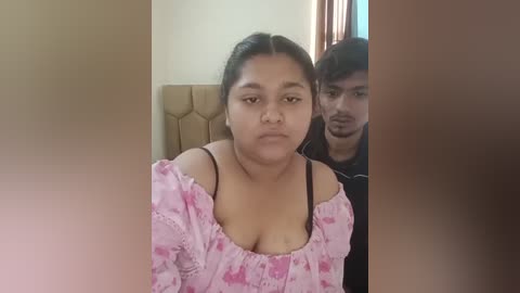 Media: Video of a plus-sized woman in a pink patterned off-shoulder top and a man in a black shirt, both sitting indoors.