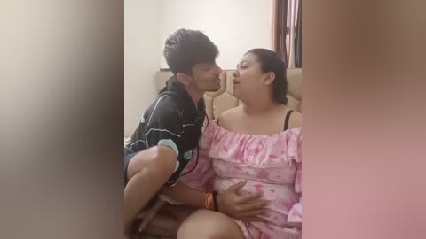 Media: Video of a South Asian couple in an intimate embrace; man in black striped shirt, woman in pink off-shoulder dress, both smiling, in a dimly lit room.