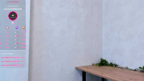 Media: Video of a minimalist room with a wooden bench against a plain white wall, featuring a digital calendar and a small plant.