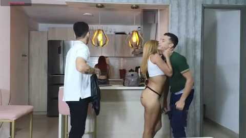 Media: Video of a modern kitchen with a man and woman kissing passionately; man wears a green shirt and jeans, woman in white crop top and thong.