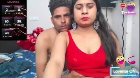 Media: Video of a shirtless man embracing a woman in a red tank top, both with South Asian features, in a bedroom with a blue bedspread.