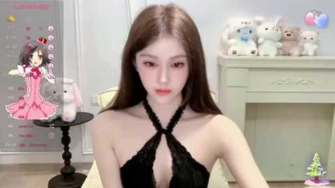 Media: Video of a slender, young East Asian woman with long brown hair and fair skin, wearing a black halter dress. Background features a calendar, stuffed animals, and a fireplace.