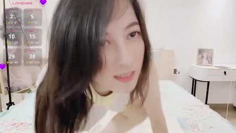 Media: Video of an Asian woman with straight, dark hair, smiling. She's in a bedroom with a bed, white walls, and a calendar.