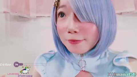 Media: A close-up video of an East Asian woman with light blue hair in a bob cut, wearing a light blue dress with puffed sleeves, smiling. Background is a soft pink curtain.