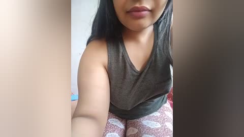 Media: Video of a South Asian woman with medium brown skin, wearing a gray sleeveless top and pink pajama pants with white polka dots. Her long, straight black hair falls over her shoulders, and she has a slight smile.