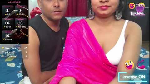 Media: Video of an Asian couple, man in black sleeveless shirt, woman in pink sari with white bra, smiling, in a bedroom setting.