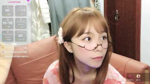 Media: A video of a young Asian woman with long brown hair, glasses, and a floral top, sitting on a brown couch, looking thoughtful.