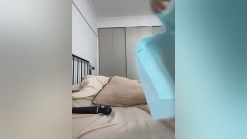 Media: A video shows a person wearing a blue shirt walking into a bedroom with beige bedding, a black vibrator on the bed, and a closet in the background.