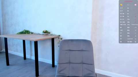 Media: A minimalist office interior with a wooden table and black legs, gray cushioned chair, light gray walls, and a digital calendar on the right wall.