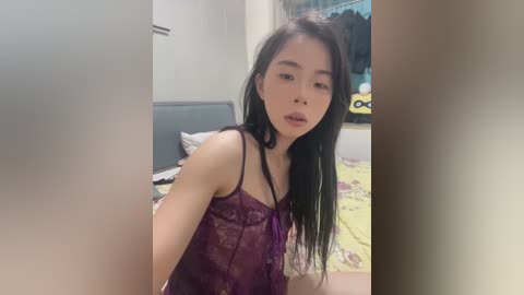 Media: A video of an Asian woman with long black hair, fair skin, and a slender physique, wearing a sheer purple lace lingerie top, standing in a bedroom with a bed and colorful wall art.