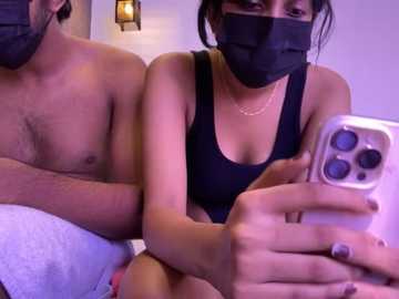 Media: Video of a shirtless man with light skin, a woman with light skin wearing a black face mask, and a black top. Both are indoors with a soft purple light, taking a selfie with a white iPhone.