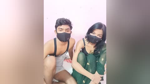 Media: A video of a South Asian couple in casual attire, wearing masks, sitting close together on a bed, with a blurred background.