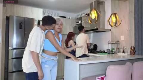 Media: A video of a modern kitchen featuring a woman in a blue crop top and jeans, and a man in a white shirt and jeans, interacting with a younger man in a white shirt.