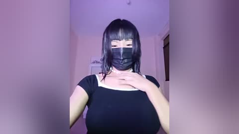 Media: A video of an Asian woman with long black hair, wearing a black mask and a black top, standing in a dimly lit hallway.