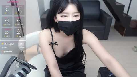 Media: A video of an East Asian woman with long black hair, wearing a black face mask, black camisole, and sitting at a desk with a computer monitor displaying a calendar.