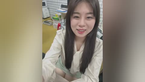 Media: A video of an Asian woman with long black hair, wearing a white lab coat, sitting at a desk with medical supplies and equipment in a clinical setting.