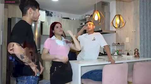 Media: A video shows a man with tattoos, a woman with red hair, and another man in a kitchen; both men wear white T-shirts, while the woman wears a pink top and black skirt.