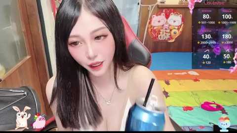 Media: A video of an East Asian woman with long black hair, wearing a blue tank top, sitting on a colorful rug in a playful room.