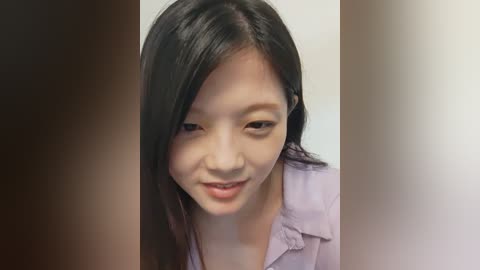 Media: Video of a smiling young Asian woman with long black hair, wearing a light purple button-up shirt, against a blurred, neutral background.