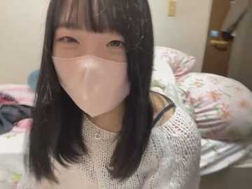 Media: Video of an Asian woman with long black hair, wearing a white knit sweater and a pink face mask, in a bedroom with floral-patterned bedding.