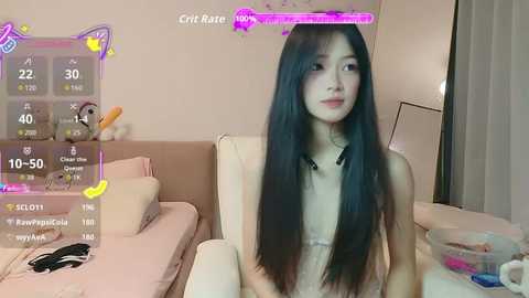 Video of an Asian woman with long black hair, wearing a light pink bralette, sitting on a beige sofa in a cozy, minimalist room.