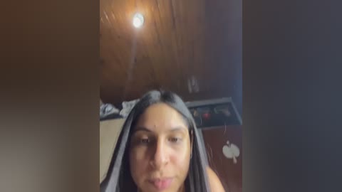 A blurry video shows a woman with medium skin tone and dark hair, wearing a gray shirt, in a dimly lit room with a wooden ceiling and an Apple logo.