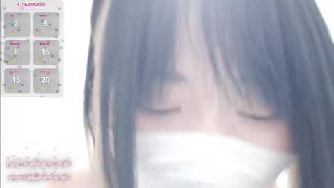 Video of a young Asian woman with straight black hair, wearing a white face mask, eyes closed, with a blurred background. The image also includes a calendar with highlighted dates.