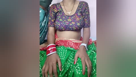 Media: Video of a South Asian woman in a colorful floral blouse and green sari with red and white polka dots, seated with hands on her sari.